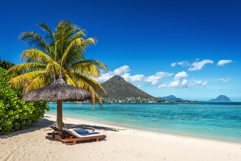 lounge chairs on a white sand beach looking at crystal blue water with mountains in the background
